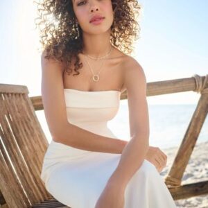 Woman in white strapless gown, beach setting.